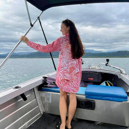 Woman in a 'Fish Feeder Wear' pink fishing dress standing on a boat with a scenic background in Australia