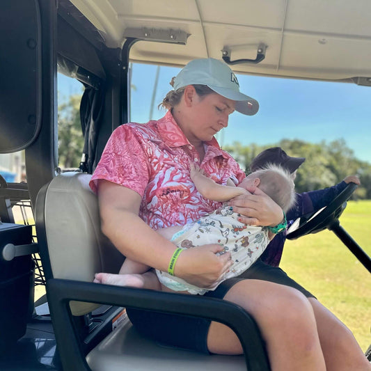 Woman holding a baby in a golf cart breastfeeding while playing sport