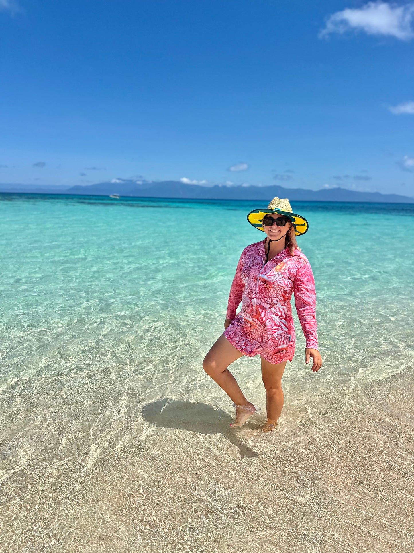 Woman in a 'Fish Feeder Wear' pink fishing dress with nursing zip and hat standing in clear turquoise water with a blue sky on the Great Barrier Reef in Australia