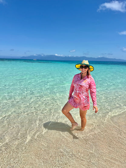Woman in a 'Fish Feeder Wear' pink fishing dress with nursing zip and hat standing in clear turquoise water with a blue sky on the Great Barrier Reef in Australia